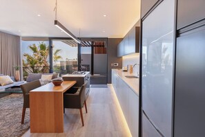 A modern kitchen with a dining area, large windows, and a view of palm trees.