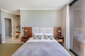 A hotel room with a large bed, wooden headboard, two bedside tables with lamps, and a sliding glass door to the outside.