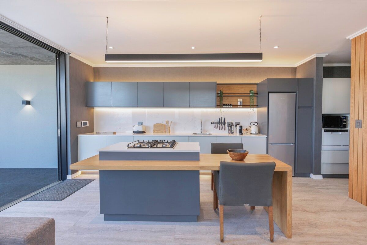 A modern kitchen with a central island, built-in appliances, and a dining area with a table and chairs.