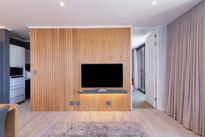 A modern living room with a flat-screen TV mounted on a wooden panel wall, a built-in entertainment unit, and a neutral-toned carpet. - Luxurious Beach Escape in Bloubergstrand (Cape Town)
