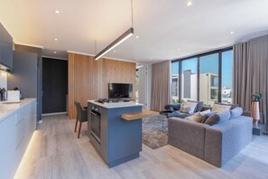 A modern kitchen with a central island, a dining area with a sofa, and a large window offering a city view.