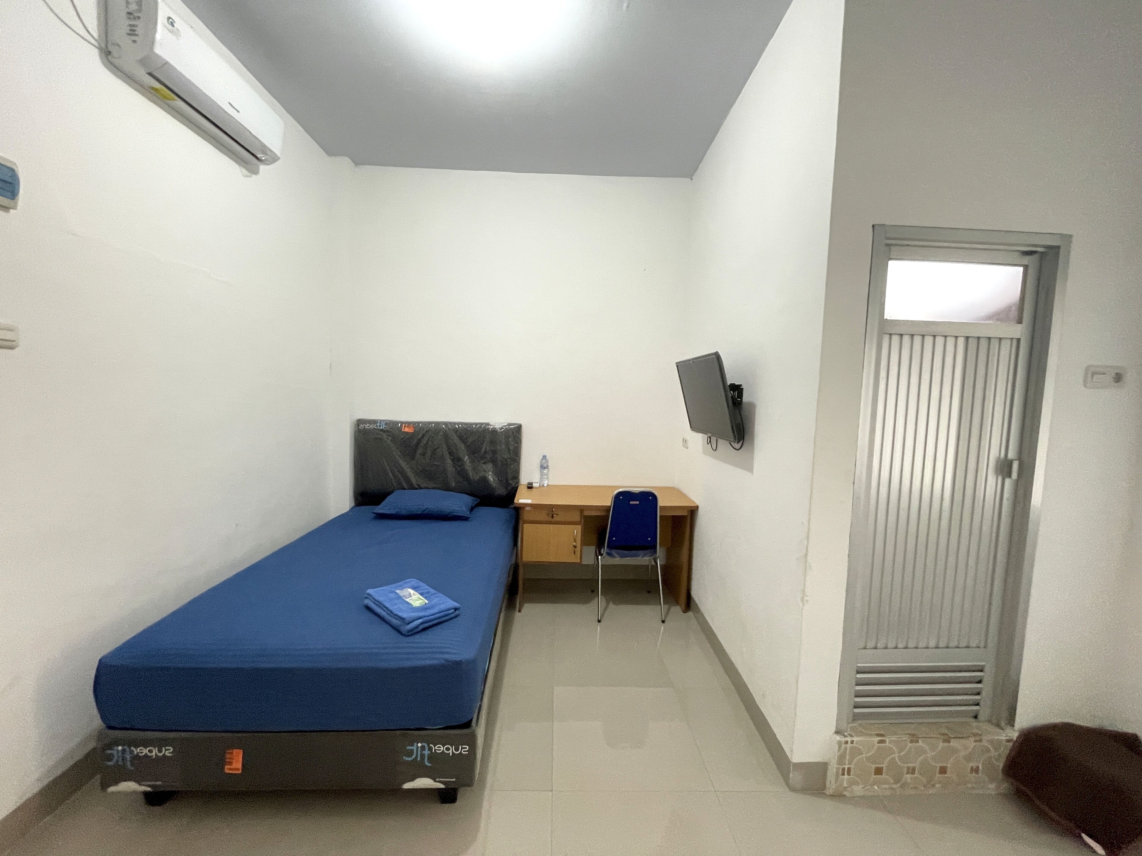 A small, clean room with a bed, a desk, a chair, a TV, and a door.