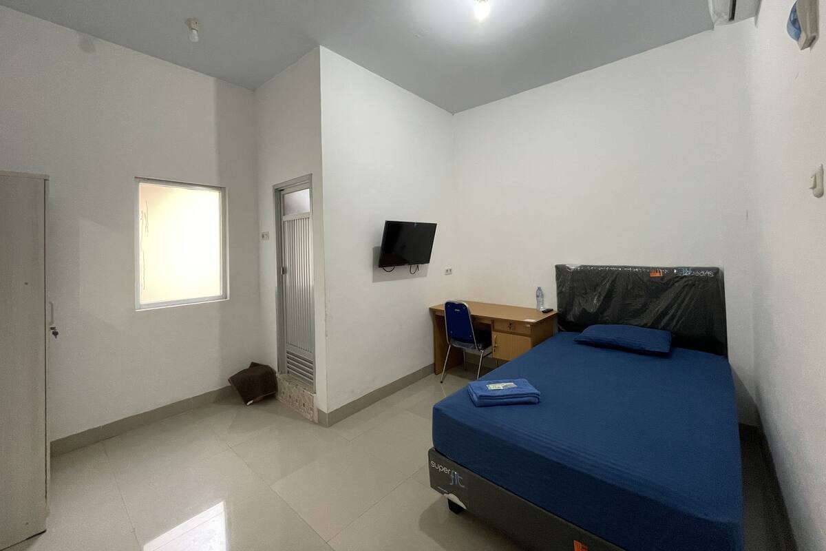 A bedroom with a bed, a desk, a chair, a television, and a door.