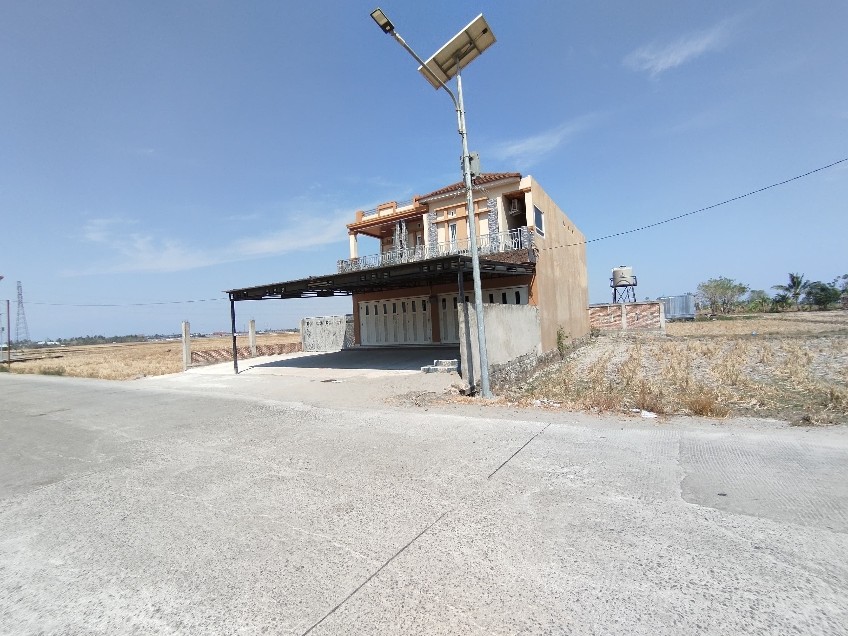 A two-story building with a balcony, a water tank in the background, and a solar panel on a pole.