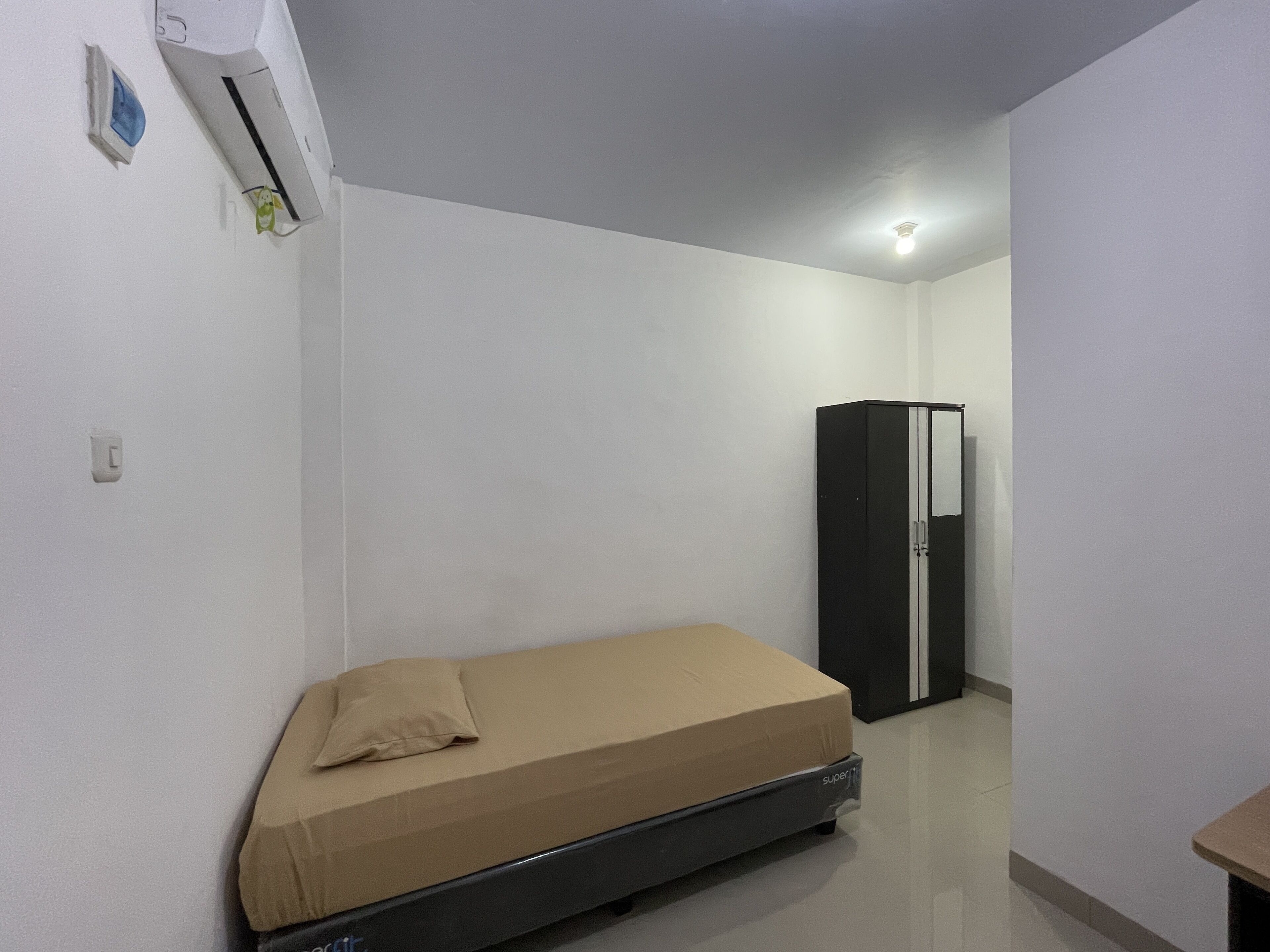 A small, sparsely furnished room with a single bed, a wardrobe, and an air conditioning unit.