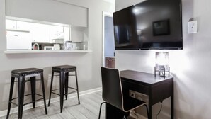 Una cocina moderna con un ventanal grande, dos taburetes de bar, una mesa de comedor y un televisor de pantalla plana montado en la pared.