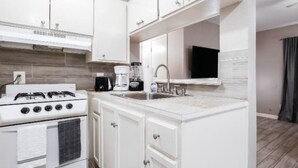 Una cocina moderna con armarios blancos, estufa a gas, cafetera y lavaplatos.