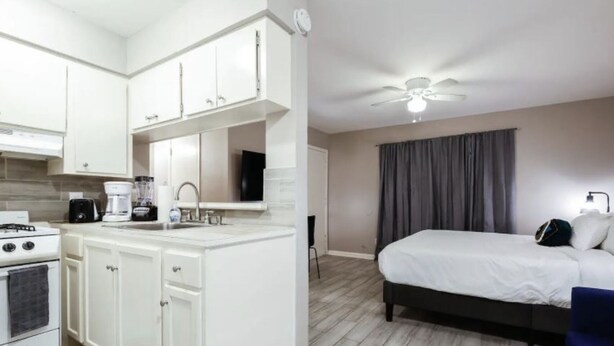 Una habitación de hotel moderna con kitchenette, una cama, un ventilador de techo y una ventana con cortinas.