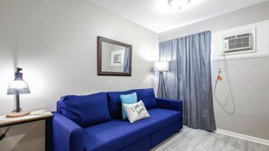 Una habitación con un sofá azul, un espejo enmarcado, una lámpara y un ventanal con cortinas.