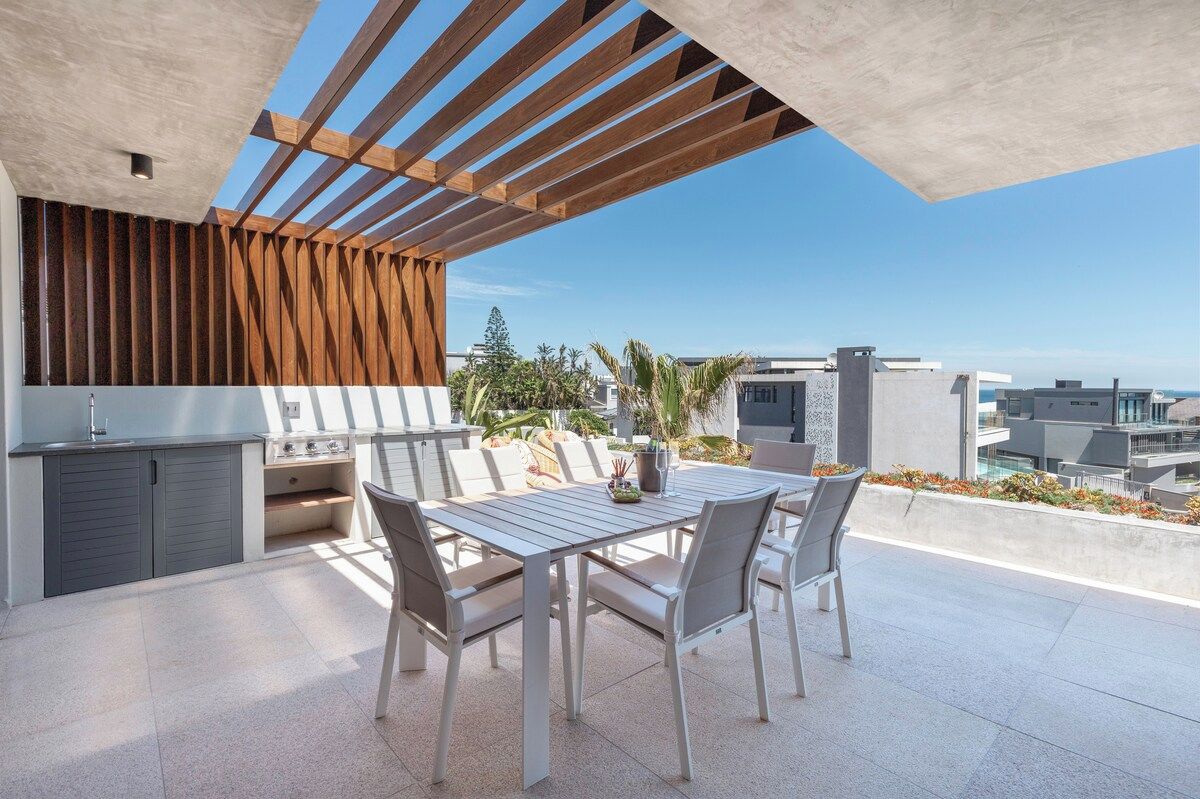 Un patio exterior con mesa y sillas, una parrilla incorporada y vistas de la ciudad.