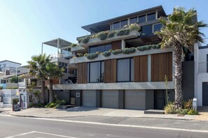 A modern multi-story building with balconies, a coffee shop, and palm trees.