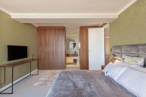 Ein Schlafzimmer mit Bett, Fernseher, einer Konsole und einem durchgehenden Türspalte sichtbaren Badezimmer.