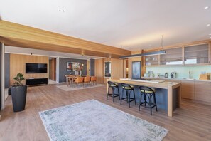 A modern kitchen with a central island, bar stools, and a dining area with a table and chairs.