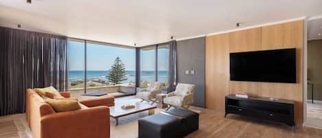 A modern living room with a large TV, comfortable seating, and a view of the ocean.