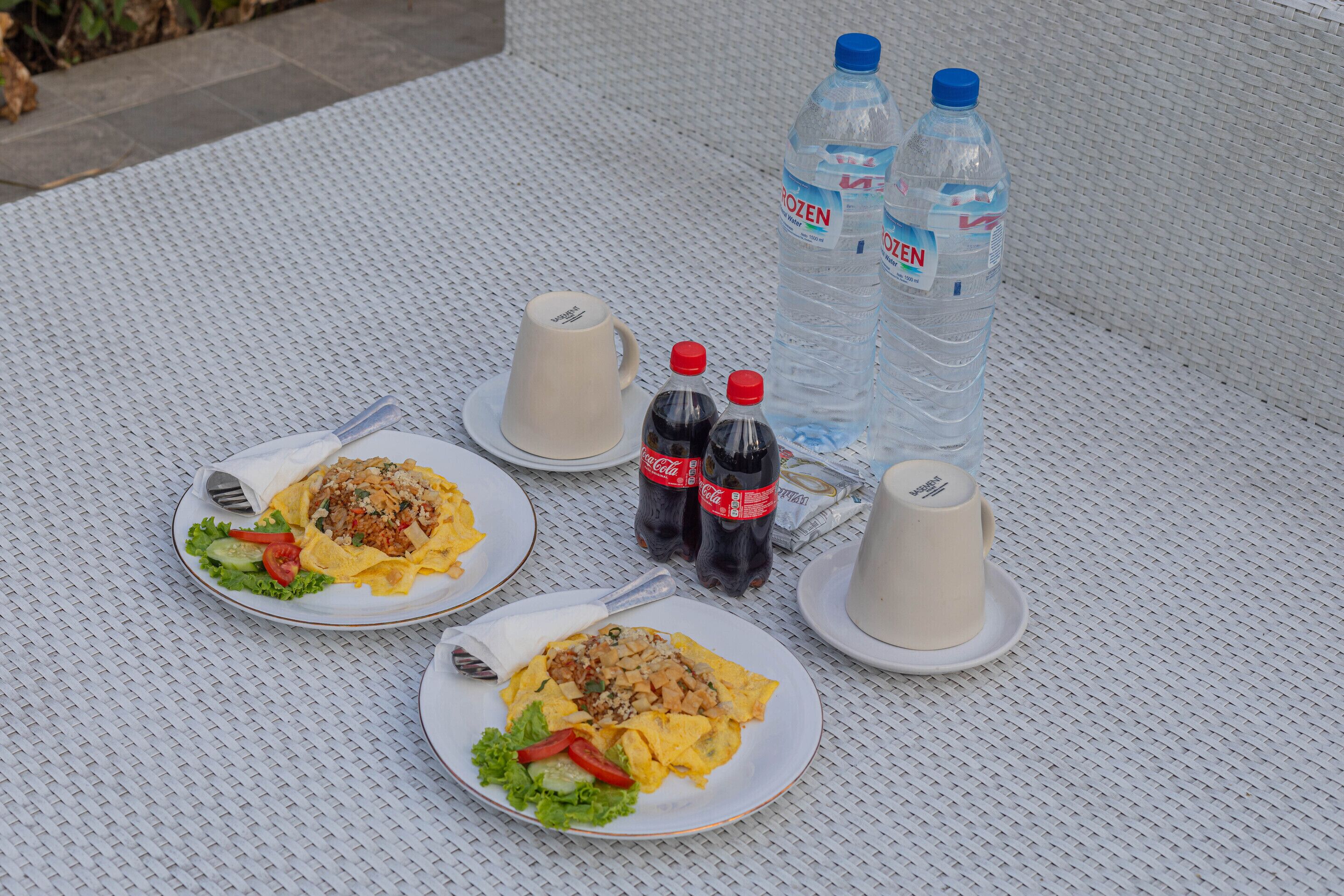 Ein Tisch mit zwei Tellern Essen, zwei Tassen, zwei Wasserflaschen und zwei Coca-Cola Flaschen.