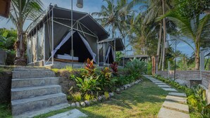 A tented accommodation with a stone staircase leading to a grassy area with plants and palm trees. - Kubu Selat Villa and Glamping (Gianyar)