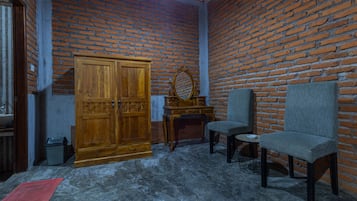 A room with a brick wall, a wooden wardrobe, a small table, two chairs, and a red rug on the floor.