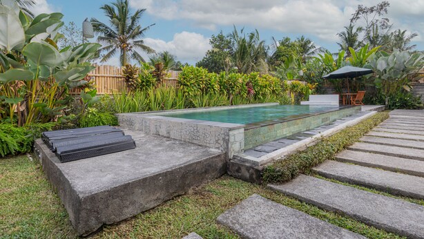 A pool area with a stone deck, surrounded by tropical plants and a wooden fence. - Kubu Selat Villa and Glamping (Gianyar)