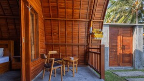 A wooden cabin with a balcony, a bed, a table, and chairs. - Kubu Selat Villa and Glamping (Gianyar)