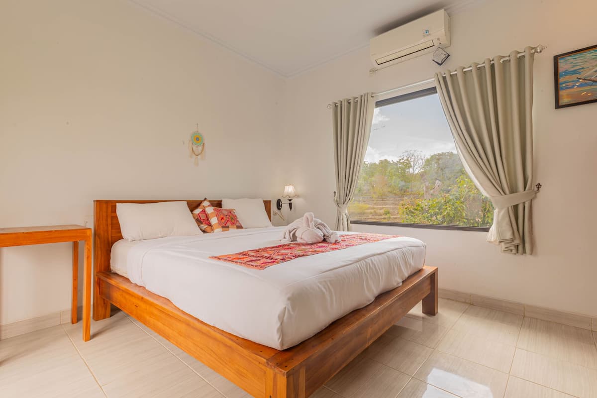 A bedroom with a wooden bed, a bedside table, a window with curtains, and an air conditioning unit.