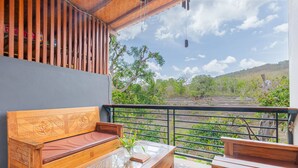 A wooden balcony with a sofa and coffee table, offering a view of a green landscape and trees. - Lahi Villa  (Penida Island)