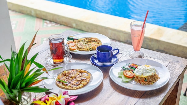 A table with plates of food, a glass of iced tea, and a blue cup, set near a pool. - Lahi Villa  (Penida Island)