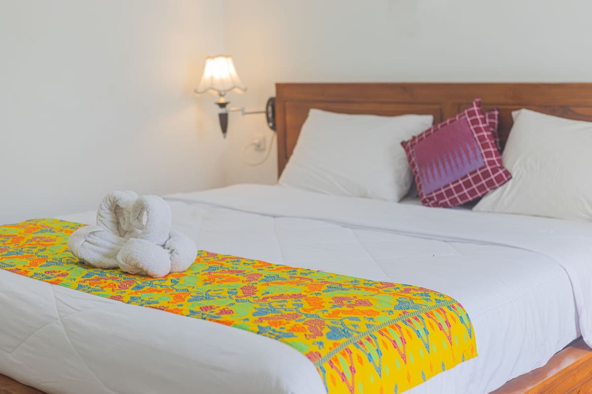A neatly made bed with a colorful blanket, white pillows, and a wall-mounted lamp.
