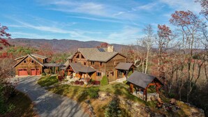 Une grande cabane en rondins, dotée de plusieurs annexes, d’une cheminée en pierre et d’un mur de soutènement en pierre agrémenté d’un espace salon extérieur.