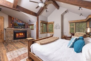 A bedroom with a fireplace, a bed with a white blanket, a wooden headboard, and a large window. - The Apex of Ski-In Ski-out Estates. Walk to Restaurants, Theater, Hot Tub, Game Tables! (Breckenridge)