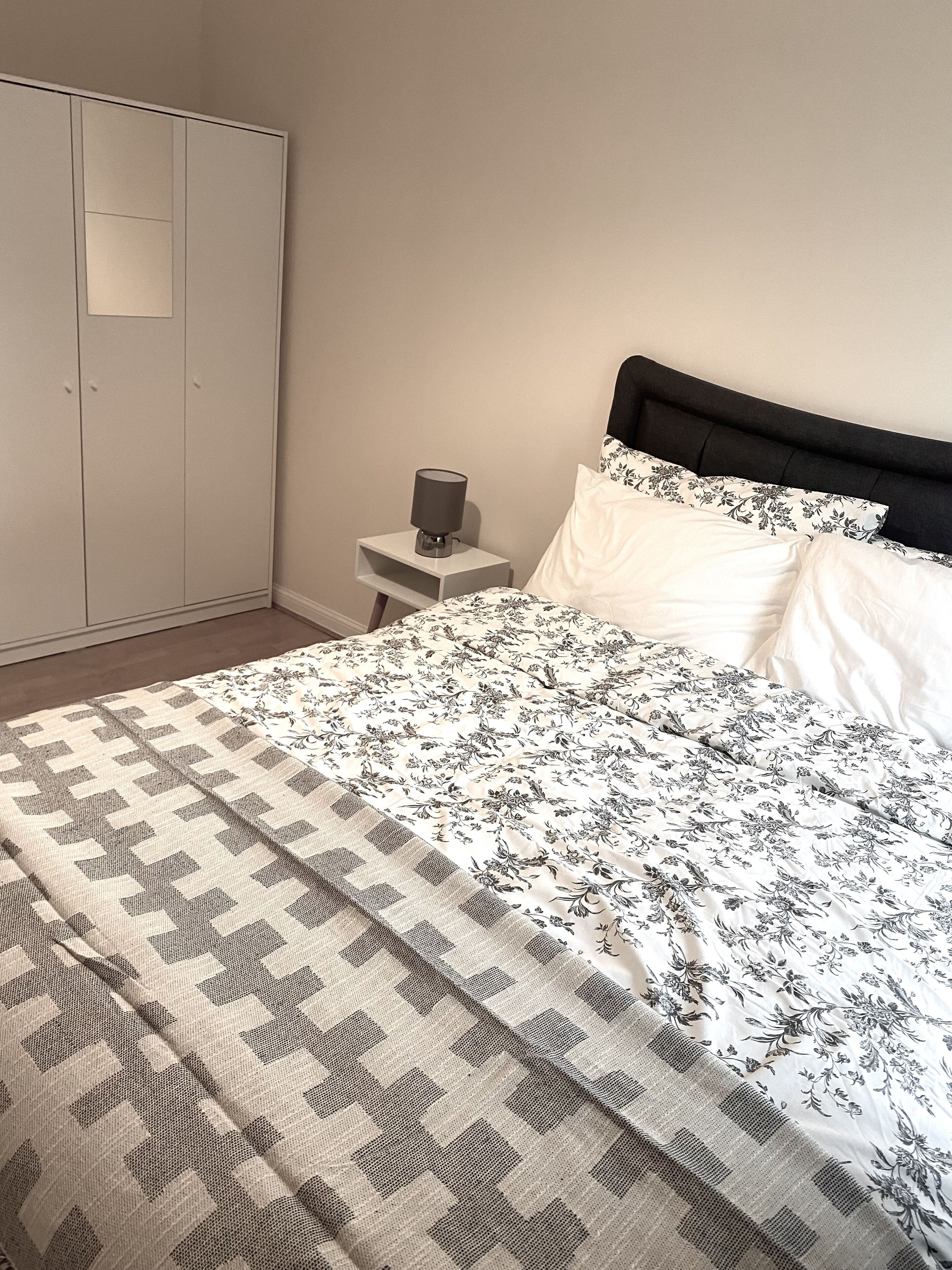 Un dormitorio con una cama, una mesita de noche, un armario y una lámpara.