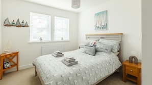 A bedroom with a bed, a nightstand, a bedside table, a window with blinds, and a wall-mounted painting.