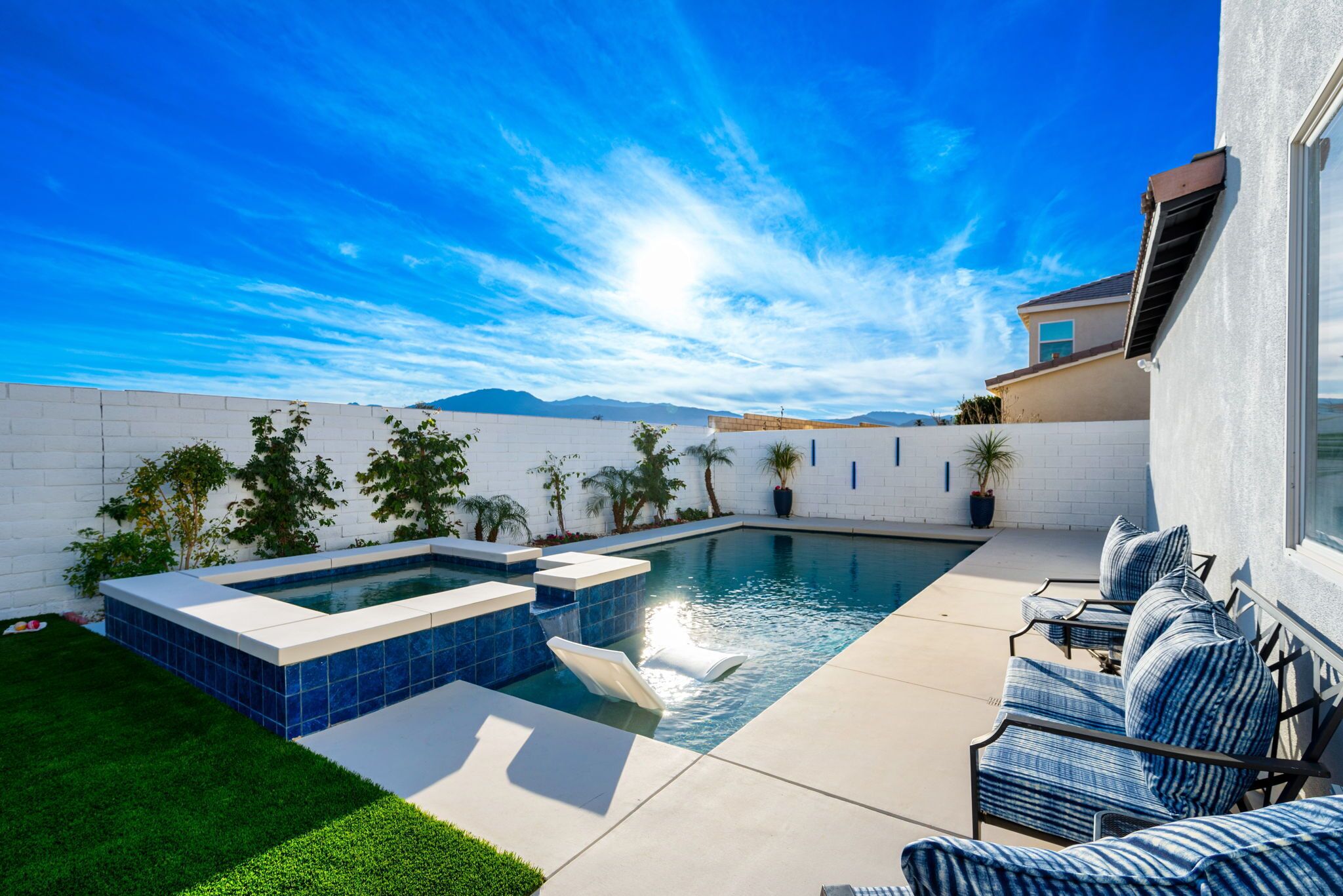 A backyard with a swimming pool, a hot tub, and a patio with lounge chairs.