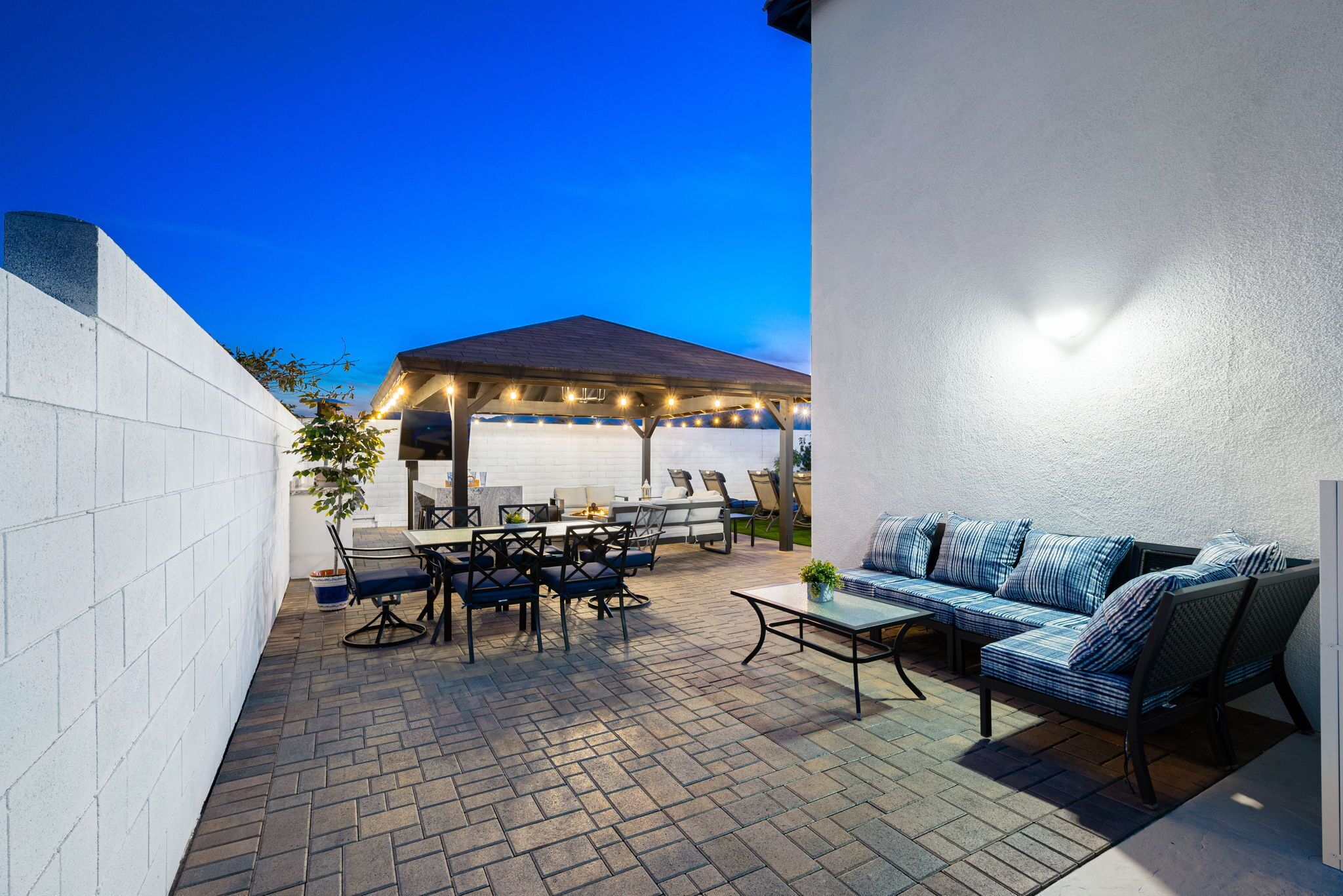 An outdoor patio with a dining area, a covered barbecue section, and a seating area with a sofa and chairs.