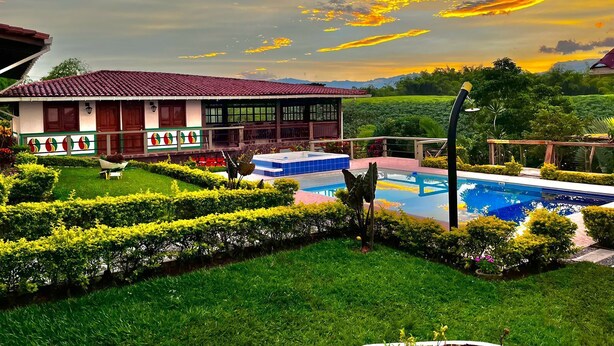 Una casa con piscina, rodeada de césped cuidado y vista a un paisaje exuberante.