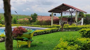 Un jardín con un pabellón, una piscina y setos bien cuidados.