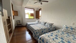 Un dormitorio con dos camas, suelo de madera, ventilador de techo y ventana con vistas a zonas verdes.