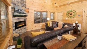 A cozy log cabin interior with a fireplace, leather sofa, wooden dining table, and a clock on the wall.