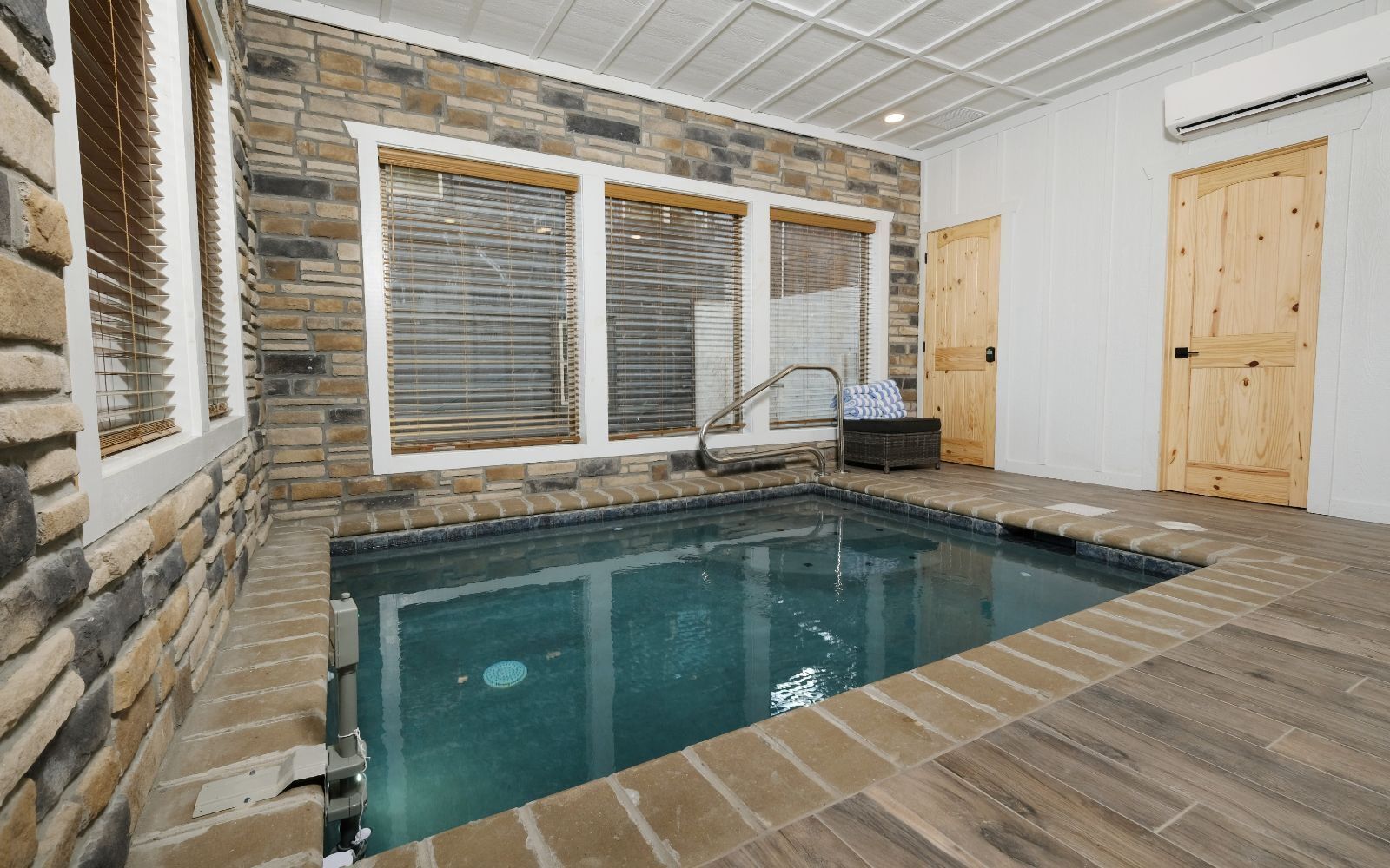 An indoor swimming pool with stone walls, wooden flooring, and a wooden door.