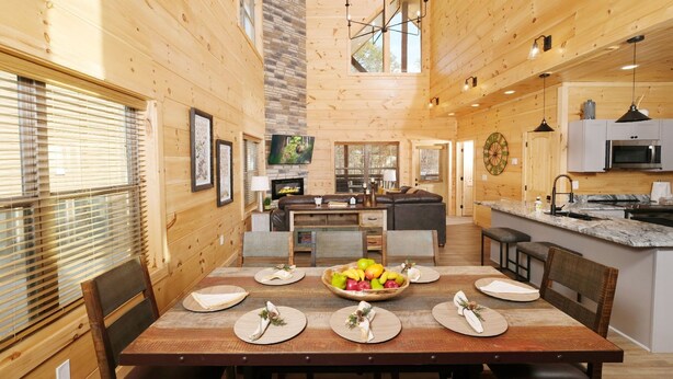 A wooden cabin interior with a dining area, kitchen, and living space.