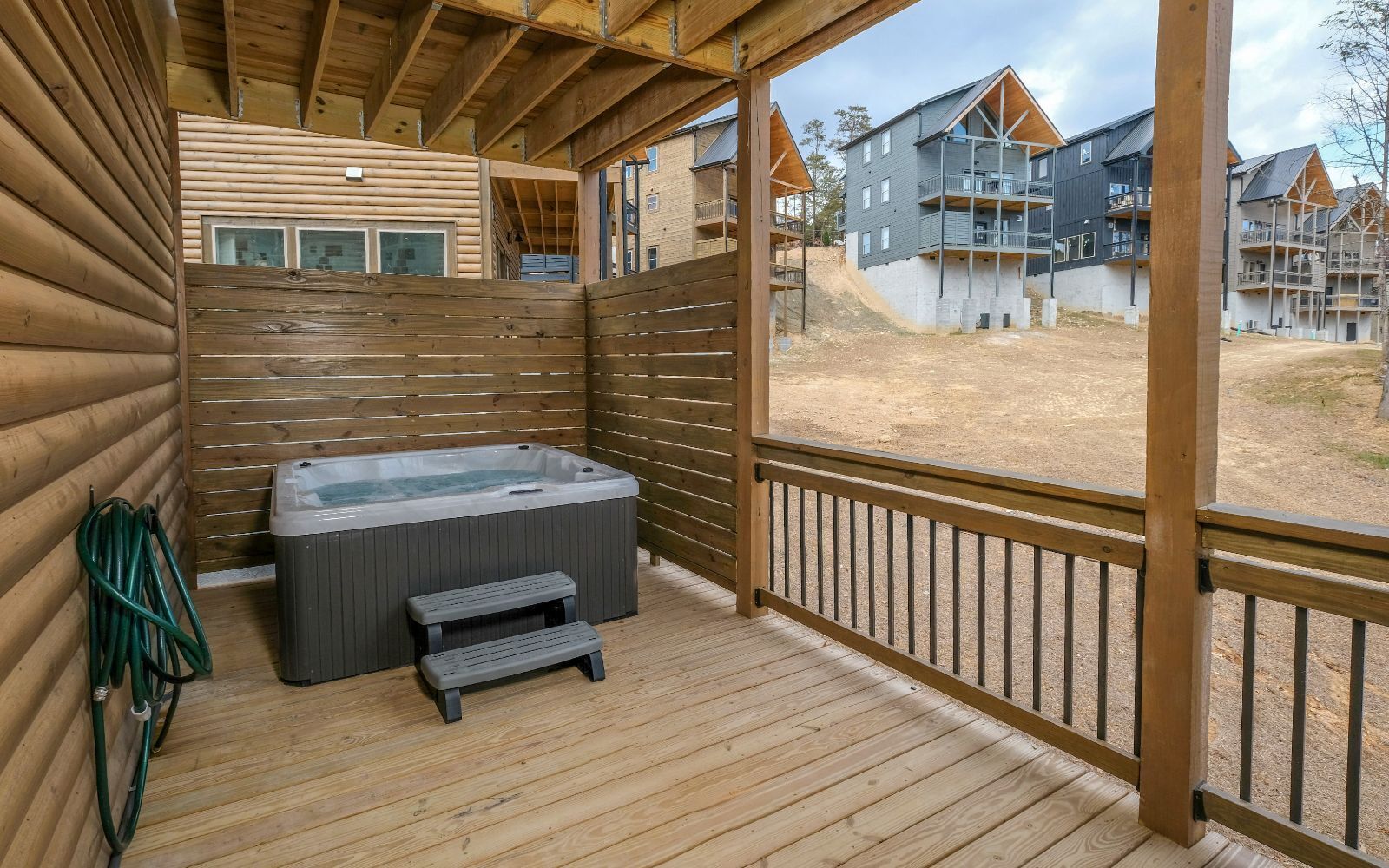 A wooden deck with a hot tub, a step stool, and a hose.