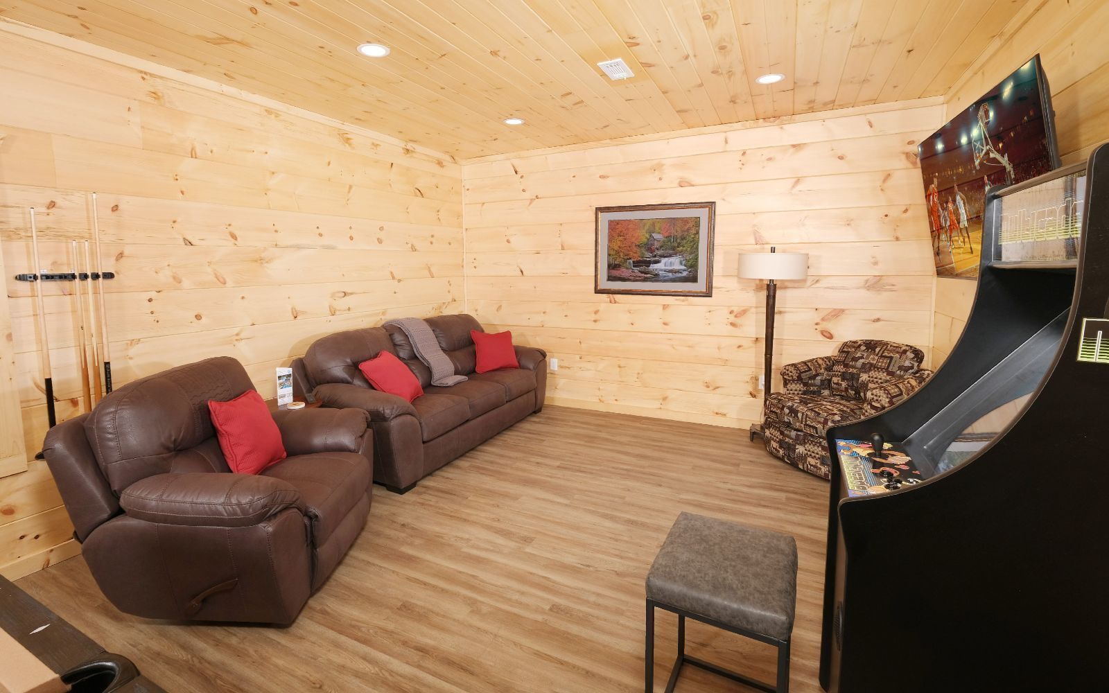 Ein gemütliches Zimmer mit einem braunen Ledersofa, einem gemusterten Sessel und einer Spielkonsole.