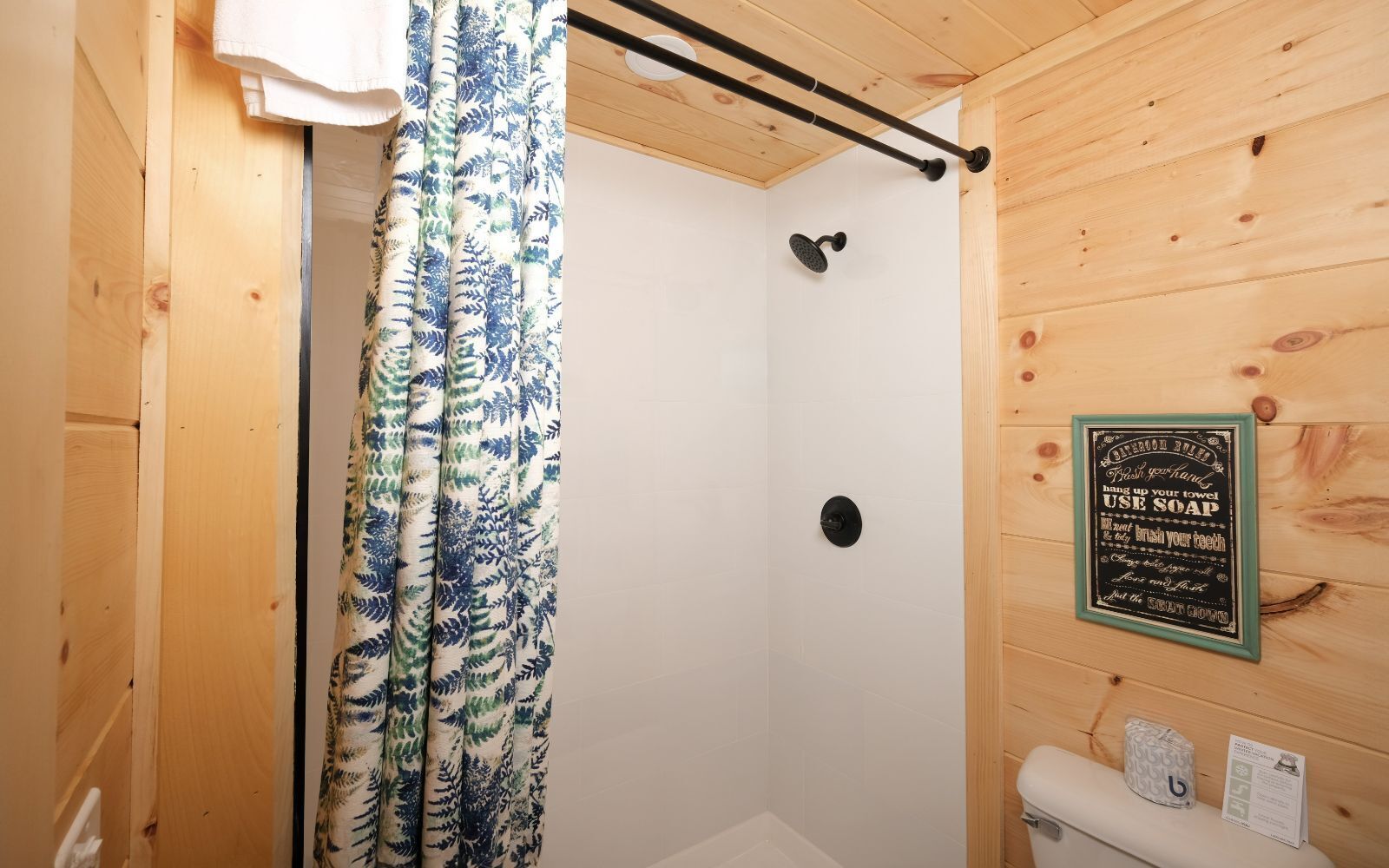 A wooden cabin bathroom with a shower, a towel rack, and a sign on the wall.