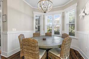 A dining area with a round table and wicker chairs, surrounded by white paneled walls and large windows with blinds. - Perfect Pitch - 4BR Naturewalk Home - Sleeps 10 - 6-Seat Golf Cart (Santa Rosa Beach)