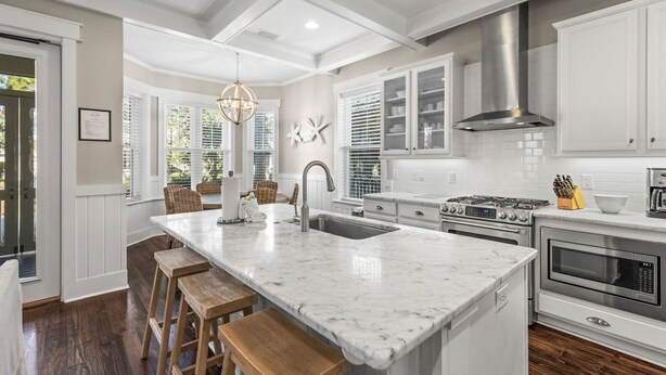 A modern kitchen with white cabinetry, a marble island, wooden stools, and stainless steel appliances. - Perfect Pitch: Your Serene NatureWalk Haven - 6 Seater Golf Cart (Santa Rosa Beach)