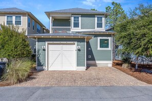 A two-story house with a garage, a balcony, and a small window. - Perfect Pitch - 4BR Naturewalk Home - Sleeps 10 - 6-Seat Golf Cart (Santa Rosa Beach)
