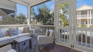 A covered outdoor area with a sofa, chair, and table, overlooking a residential area. - Perfect Pitch: Your Serene NatureWalk Haven - 6 Seater Golf Cart (Santa Rosa Beach)