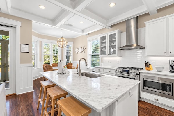 A modern kitchen with white cabinetry, a central island, wooden stools, and a stainless steel range hood.