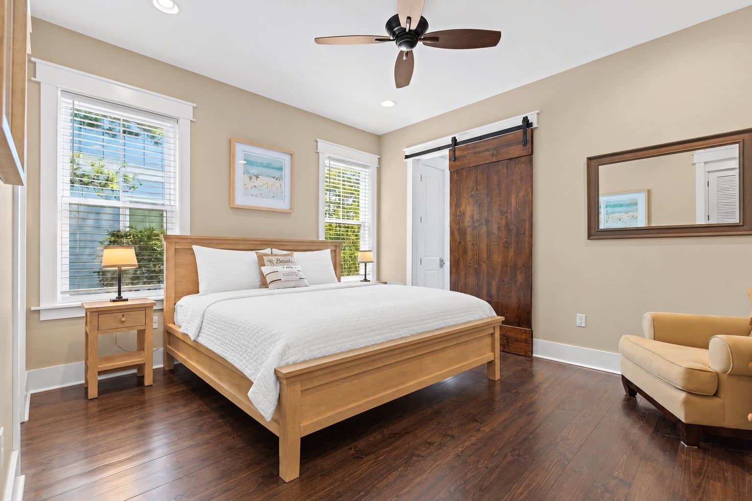 Une chambre à coucher avec un lit en bois, une table de chevet, une chaise, un ventilateur de plafond et une grande porte coulissante.