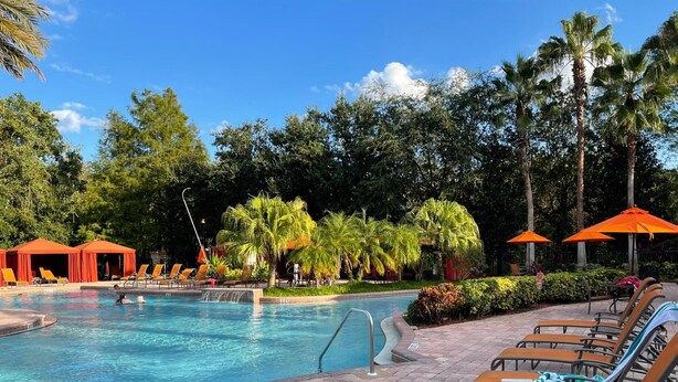 A swimming pool with lounge chairs and umbrellas, surrounded by palm trees and greenery. - Grand Superior 3BD Townhouse Near Disney (Kissimmee)