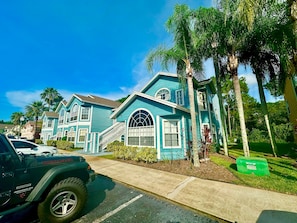 A residential area with a turquoise house, a parked SUV, and palm trees. - Grand Family Superior 3BD Condo Near Disney 21 (Kissimmee)
